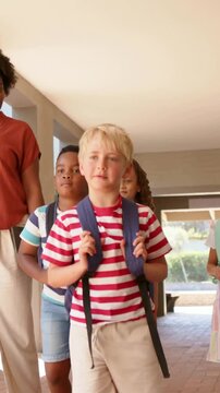Walking blonde boy holding blue backpack, leading kids through porch, adult in rust shirt guiding