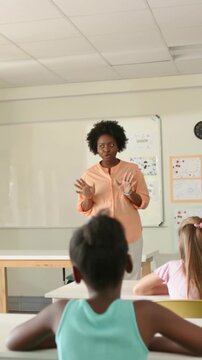 Vertical video: Raising hands, teacher gesturing and emphasizing point at whiteboard in peach top