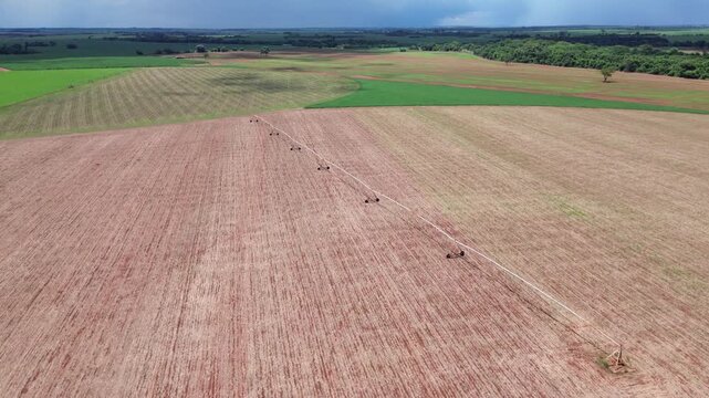 Aerial drone view of center pivot irrigation system in Brazilian rural field with dark storm clouds and rain in the background. Agriculture water management and weather concept.