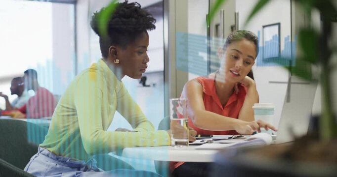 Right woman opening papers, pointing as left woman following, analyzing animated tech charts