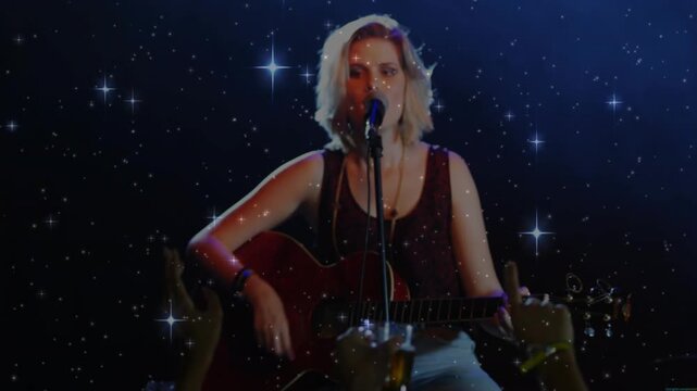 Musician strumming acoustic guitar, singing for music fans, camera focusing, starry overlay onstage