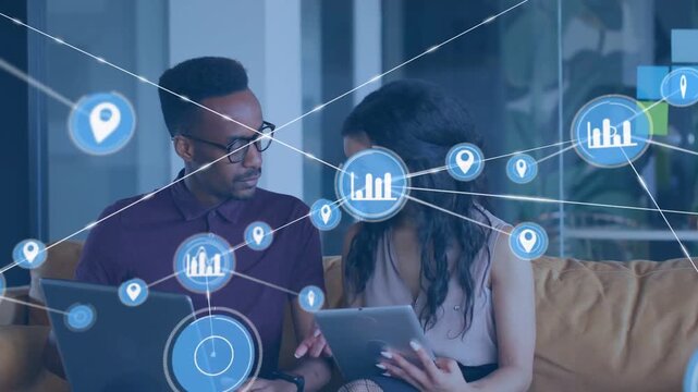 Two colleagues reviewing tablet, laptop while blue HUD icon appearing, connecting data nodes