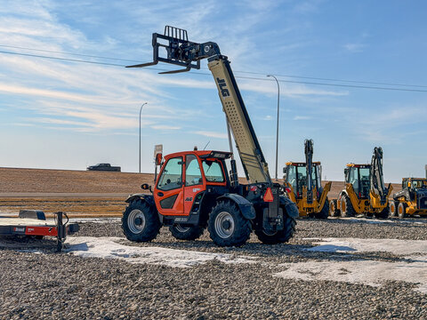 Regina, Canada - February 2026: JLG telehandler with extended boom and forks on a construction site, surrounded by heavy machinery, gravel ground, and open sky background.
