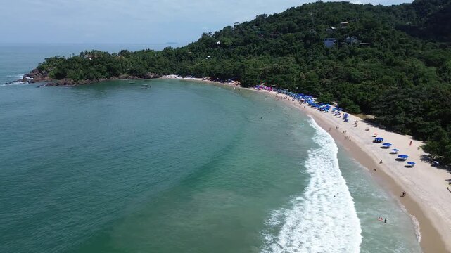 Aerial drone view of Felix Beach in Ubatuba, Brazil. Beautiful tropical coastline with turquoise water, white sand and lush green rainforest under a bright sunny blue sky.