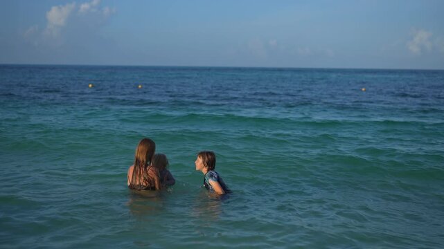 Young mom spending quality time with her two sons on a beautiful tropical beach, enjoying sunshine, laughter, and family bonding moments by the sea.