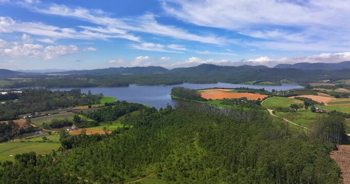 4K aerial drone view of Alto Tiete reservoir in Brazil, showing water storage, rural landscape, forests and agricultural fields under blue sky.