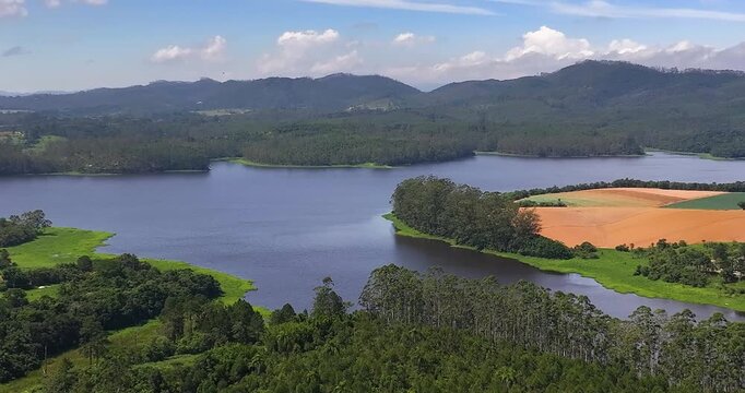 4K aerial drone view of Alto Tiete reservoir in Brazil, showing water storage, rural landscape, forests and agricultural fields under blue sky.