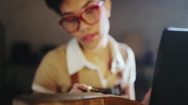 A person is painting a piece of wood in a workshop. The lighting is low and warm. The focus is on the hands and brush applying paint. The background shows tools and materials.