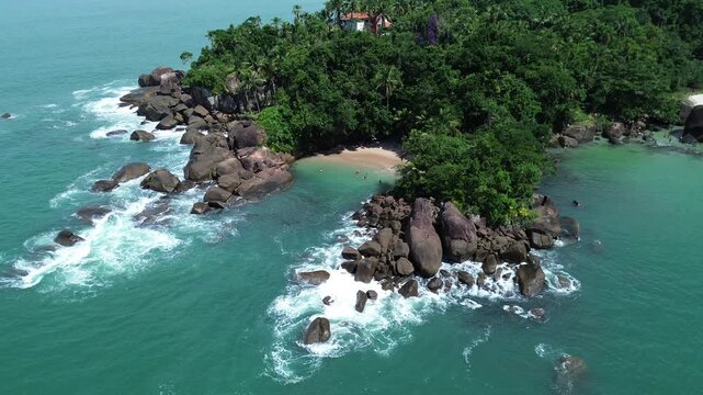 Aerial drone view of Portugues Beach in Ubatuba, Brazil. Hidden tropical cove with crystal clear turquoise water, white sand and lush rainforest coastline in Sao Paulo state.