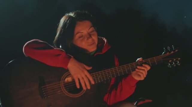 Asian woman camping guitar campfire night, solo camper musician strumming soulful acoustic tune, cozy ember glow and drifting smoke, candid closeup of smiling player leaning on instrument, intimate