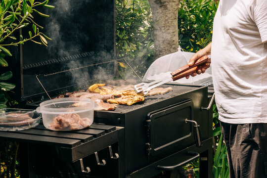 Backyard barbecue grilling meat on smoker with tongs
