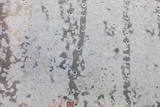 Thick condensate of small water droplets covers a transparent plastic surface or greenhouse film. The moisture texture creates an intricate pattern of streaks and bubbles, indicating high humidity and