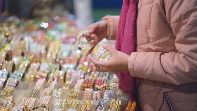 Woman buying bangles at fair market, Indian mela bangle shopping close up, Traditional bangles selection in local market, Female hands choosing colorful bangles stock video.