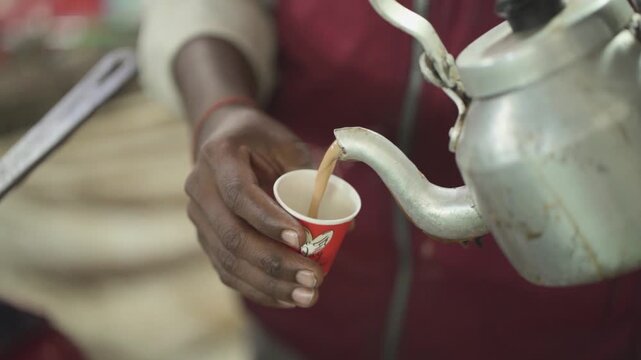 Street vendor pouring hot chai, Close up of tea being served in cup, Indian roadside chai preparation scene, Hot milk tea served from kettle stock video.