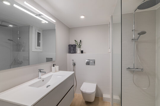 Modern bathroom with a sleek design. Features a white vanity, mirror, shower, and toilet. Bright lighting enhances the clean aesthetic.