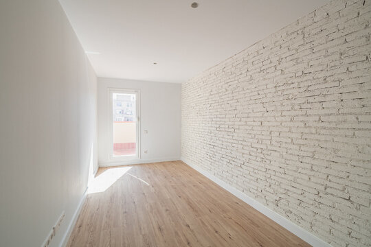 Empty room with white brick wall and wooden floor. Natural light enters through the door, creating a bright and spacious atmosphere.