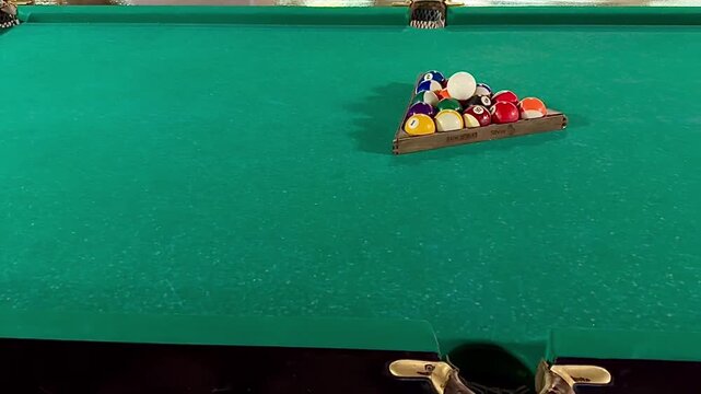 Slow camera dolly movement over a green felt billiard table shows the colorful balls neatly arranged in a triangle rack, ready for the break shot to start the game