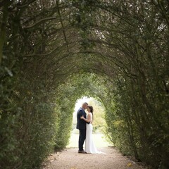 Fototapeta premium Wedding couple caucasian adult bride groom tunnel archway intimate embrace outdoor ceremony lush greenery romantic moment bridal gown suit