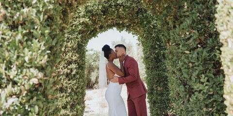 Fototapeta premium Adult male female couple kissing under green arch hedge wedding dress red suit