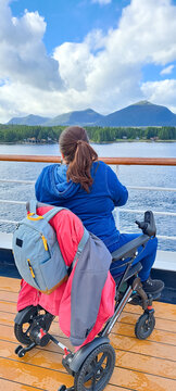 Young woman in a wheelchair sits looking out over the ocean from the deck of a cruise ship, travelling in Alaska, enjoying the freedom from disability the mobility aid allows her to travel.
