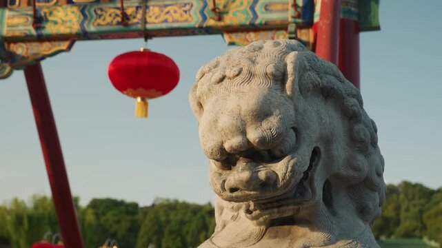 Stone guardian lion statue with red lanterns and ornate arch, park trees and distant pagoda, daytime sunlight, closeup frontal view capturing carved texture and weathered stone, serene festival mood,