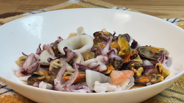 Mix of boiled seafoods in white bowl on checkered napkin