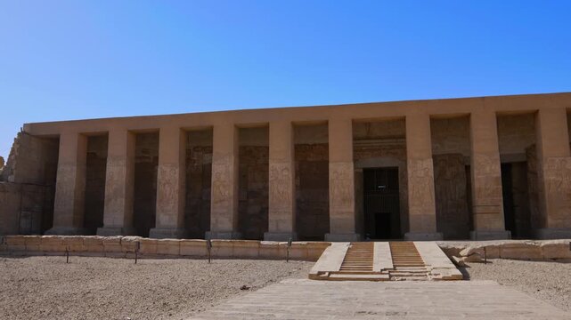 Abydos Temple of Seti I facade with grand stairway and colonnade in Egyptian desert. One of Egypt's most sacred ancient sites under vivid blue sky. Egypt.
