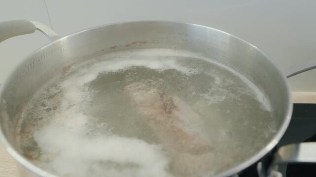 Boiling water in a pot with meat during cooking process on a stove in a kitchen