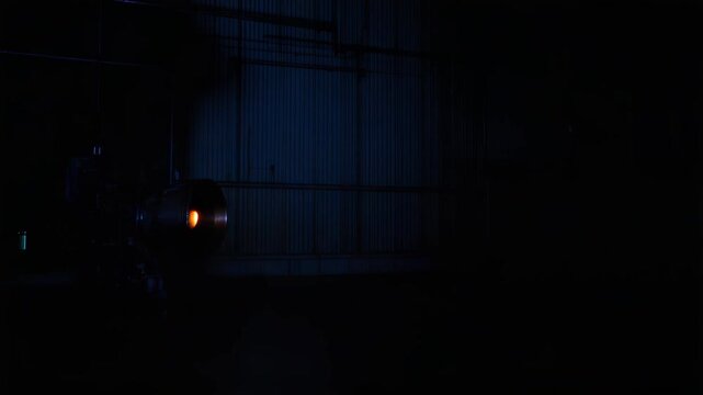 Rocket engine test firing in a dark industrial facility, generating a bright blue flame and high velocity exhaust for propulsion research and development