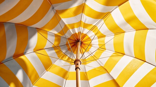 Yellow and white striped beach umbrella viewed from underneath, showcasing the intricate pattern and structure of the canopy and pole against a clear sky