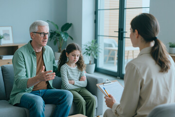 Obraz premium Senior man discussing concerns with therapist while girl sitting beside him during counseling session. Family therapy concept for mental health services, medium shot