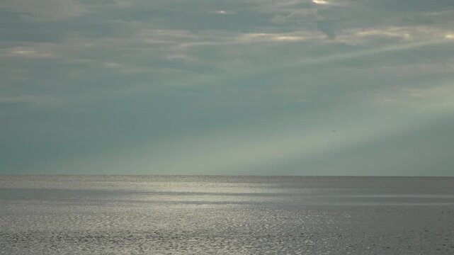 Sunbeams ocean horizon dramatic light rays pierce through dark clouds over the tranquil sea landscape