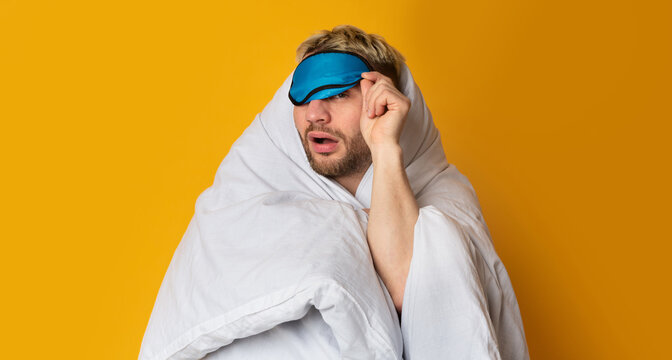 Funny guy wrapped in blanket takes off his sleep mask and squints