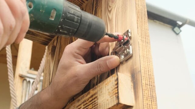 Furniture assembly worker s hands using electric screwdriver to attach door hinge to new wooden cabinet. Worker assembling cabinet. Custom-made furniture production.