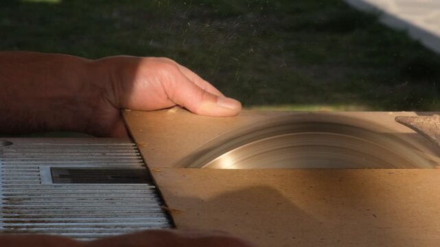 Carpenter hands using stationary circular saw to cut hardboard during furniture production. Carpenter cutting hardboard sheet on electric circular saw without gloves. Material cutting for construction