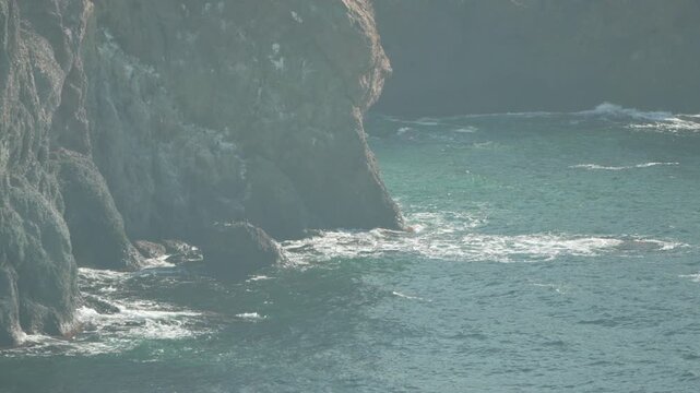 Cliffs ocean waves crashing against rugged atlantic coastline rocks on a sunny, hazy day, showing raw natural beauty.