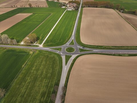 Aerial View of a Roundabout: An aerial perspective showcases a modern roundabout connecting rural roads amidst vibrant green fields and dry earth, illustrating efficient transportation infrastructure.