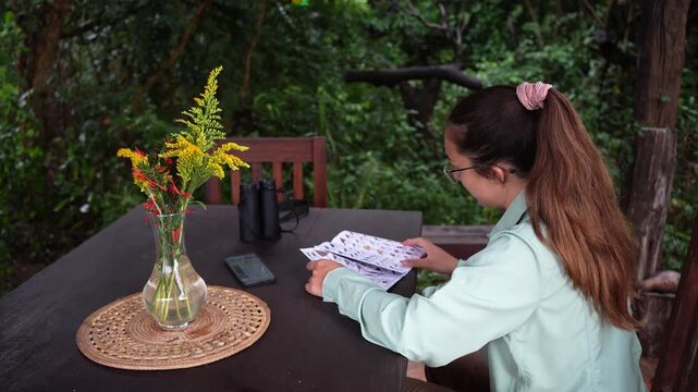 Young ornithologist woman identifying birds with a field guide