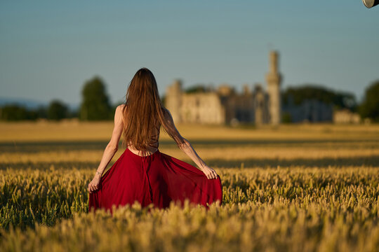 Woman rye field red dress. Happy woman in a long red dress in a beautiful cornfield. Old caste ruins in the background