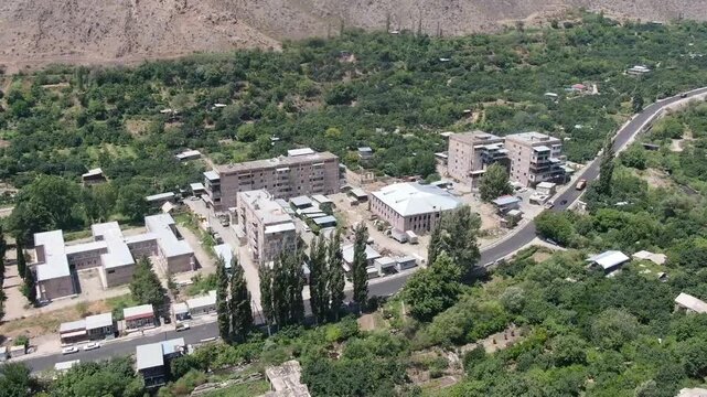 Aerial drone view of a city located in a deep valley surrounded by tall mountains. A river runs through the town center on a cloudy day in summer.