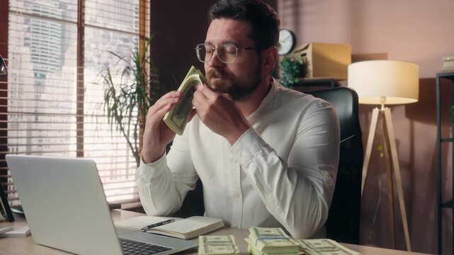 Wealthy smiling Caucasian business man holding stack dollars happy male mature businessman accountant smelling cash money earnings salary banknotes working laptop freelance office worker finance gain