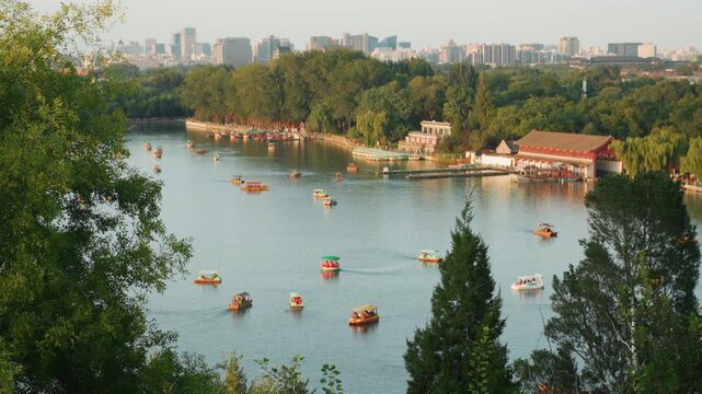 Bustling lake dotted with rental boats, treeframed shoreline and redroofed pavilion, clusters of paddleboats and small motorboats drifting under warm afternoon sun, families and tourists enjoying