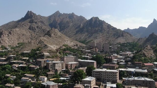 Aerial drone view of a city located in a deep valley surrounded by tall mountains. A river runs through the town center on a cloudy day in summer.