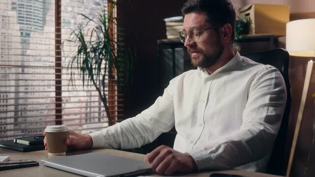 Successful Caucasian business man drinking coffee starting work typing laptop inside office CEO businessman manager opening computer begin day developer morning routine corporate workplace tech job