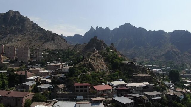 Aerial drone view of a city located in a deep valley surrounded by tall mountains. A river runs through the town center on a cloudy day in summer.