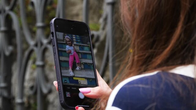 Mom taking a smartphone portrait of her daughter on tiled stairs