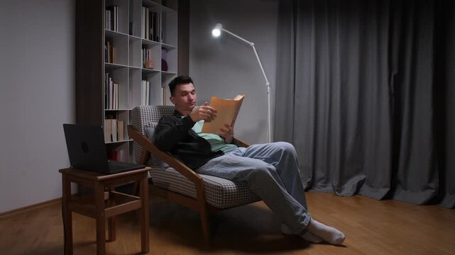 Middle aged man yawning in an armchair while reading late at night, looking tired and relaxed at home after a long day, cozy and drowsy during quiet evening reading time