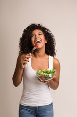 Laughing african american woman eating healthy salad over light background