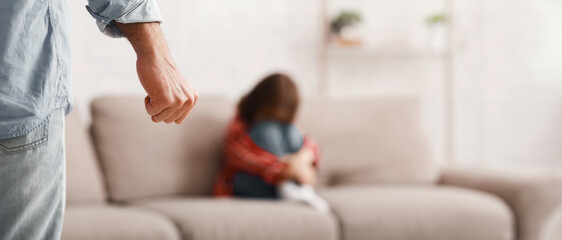 Close up of man fist and crying little girl sitting on sofa, child abuse concept