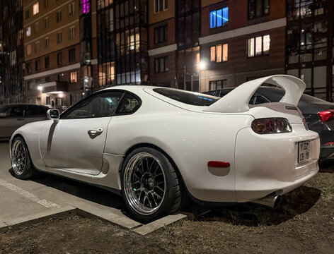 White Japanese sport car Toyota Supra IV A80 3.0 AT Turbo Sport Roof  at night the city street. Exterior of a Japanese two-door sport coupe Toyota Supra Turbo IV on parking lot. The legendary JDM car.